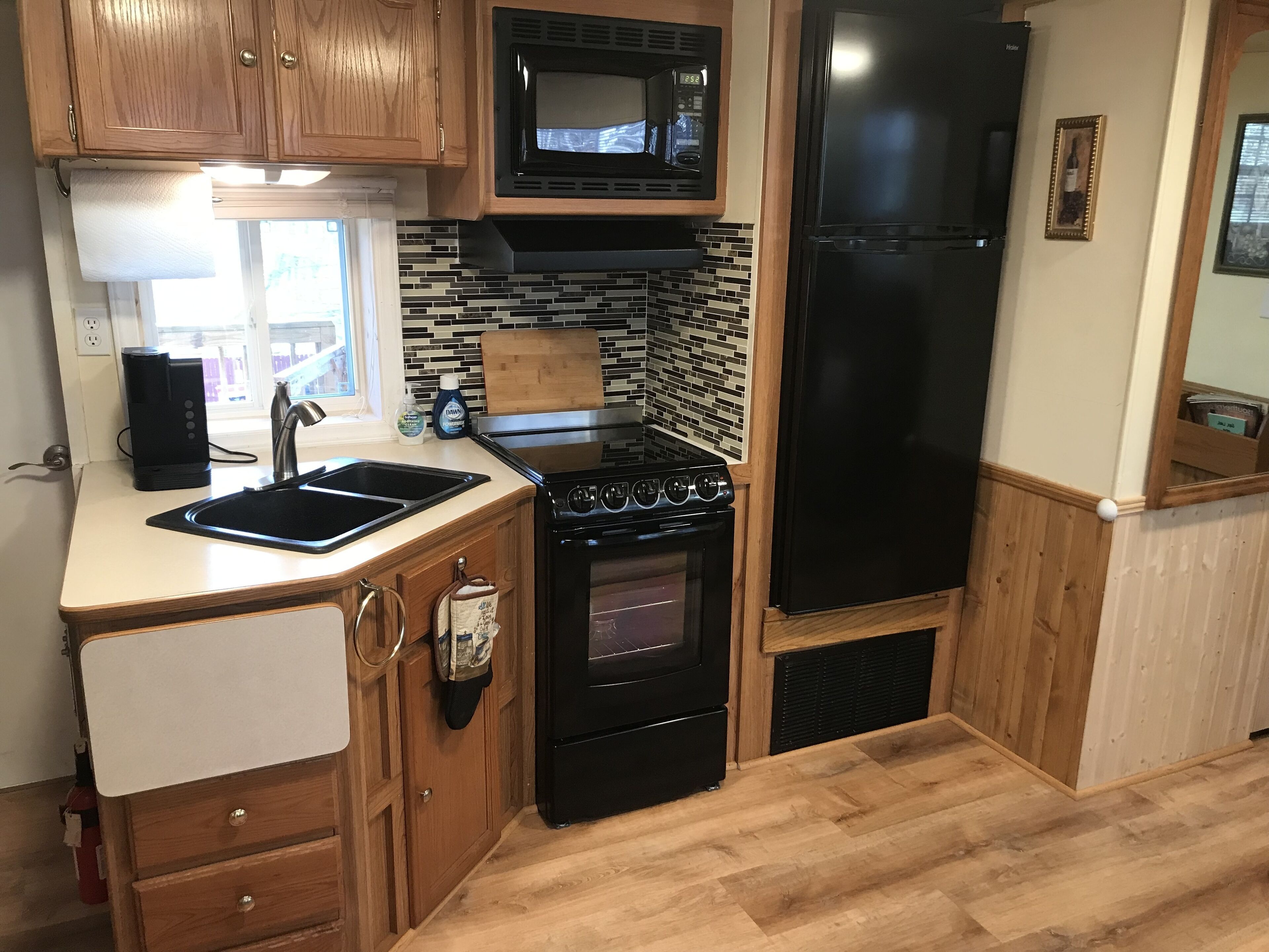 A compact kitchen with wooden cabinets, a black microwave, a refrigerator, a stove, and a sink.