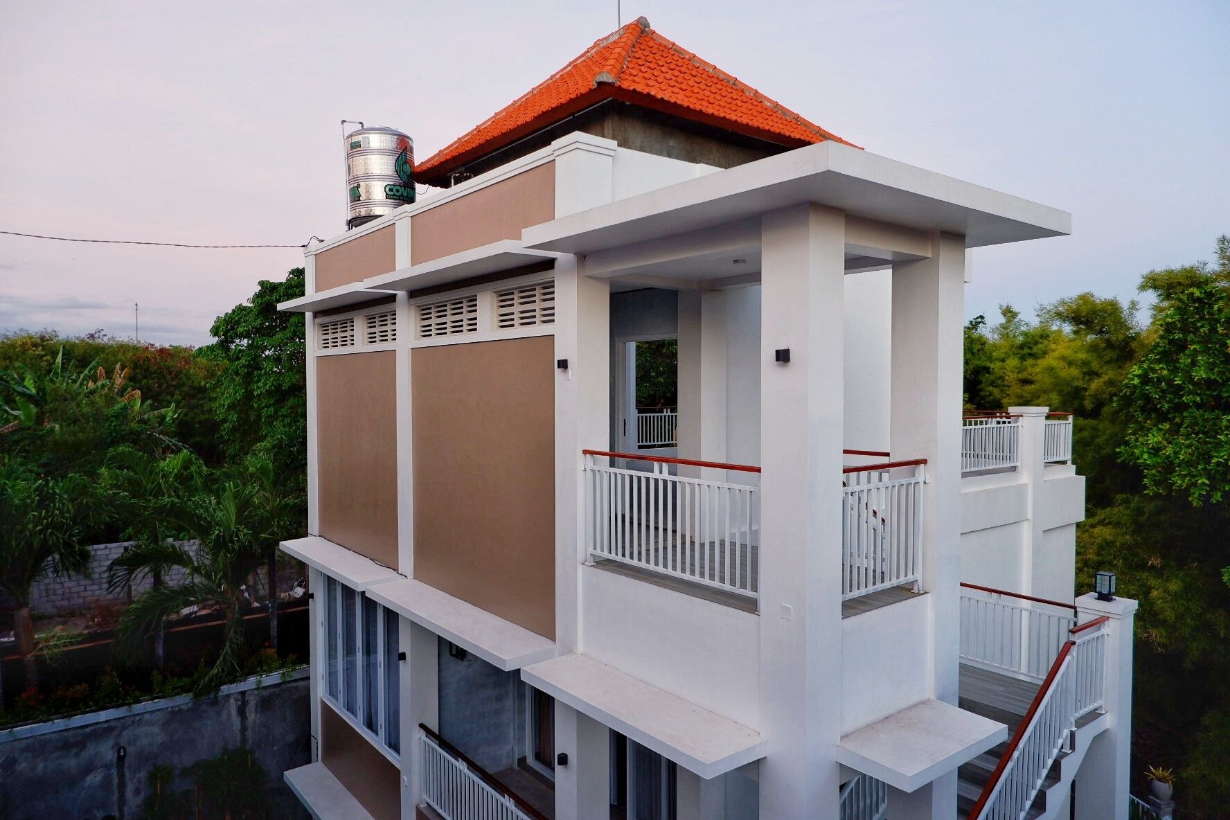 A multi-story building with a red-tiled roof, white exterior walls, and balconies with white railings.