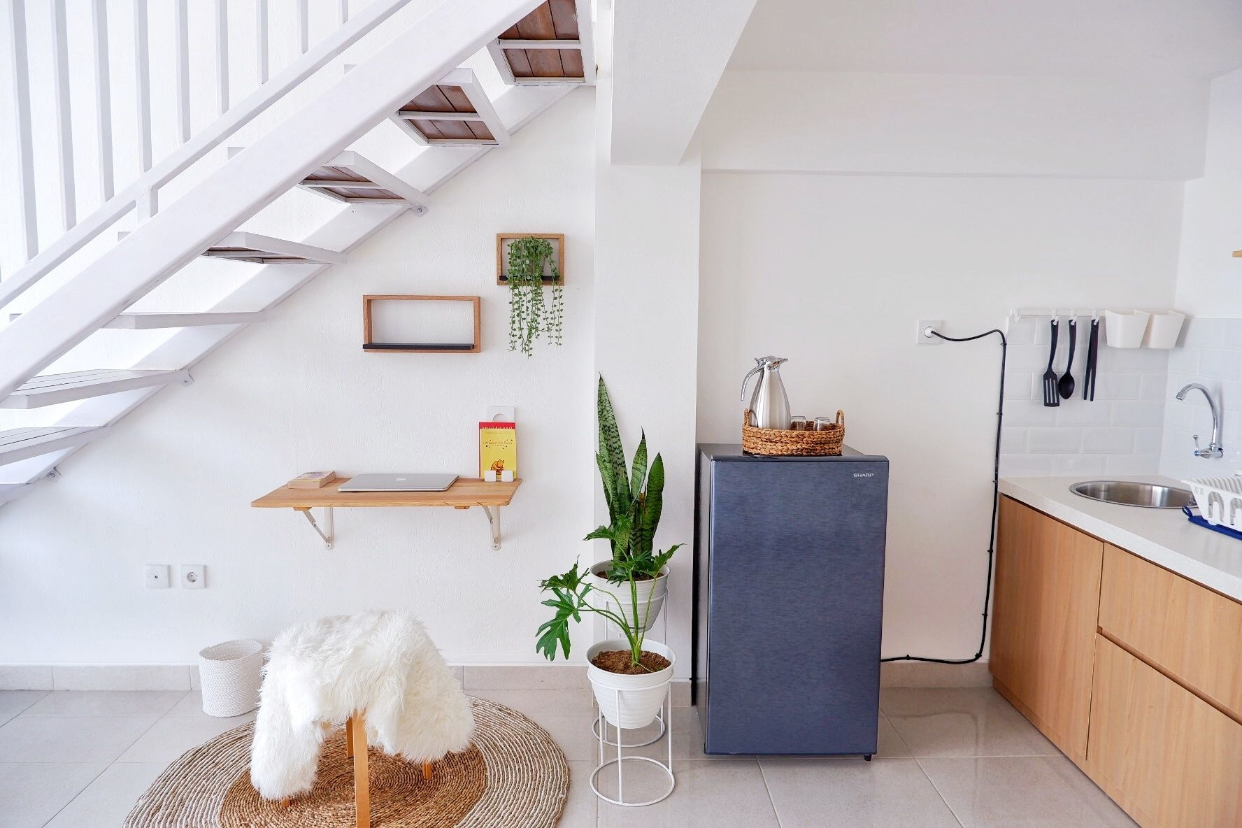 A modern kitchen with a built-in refrigerator, a wooden shelf, a hanging plant, and a white fluffy chair.