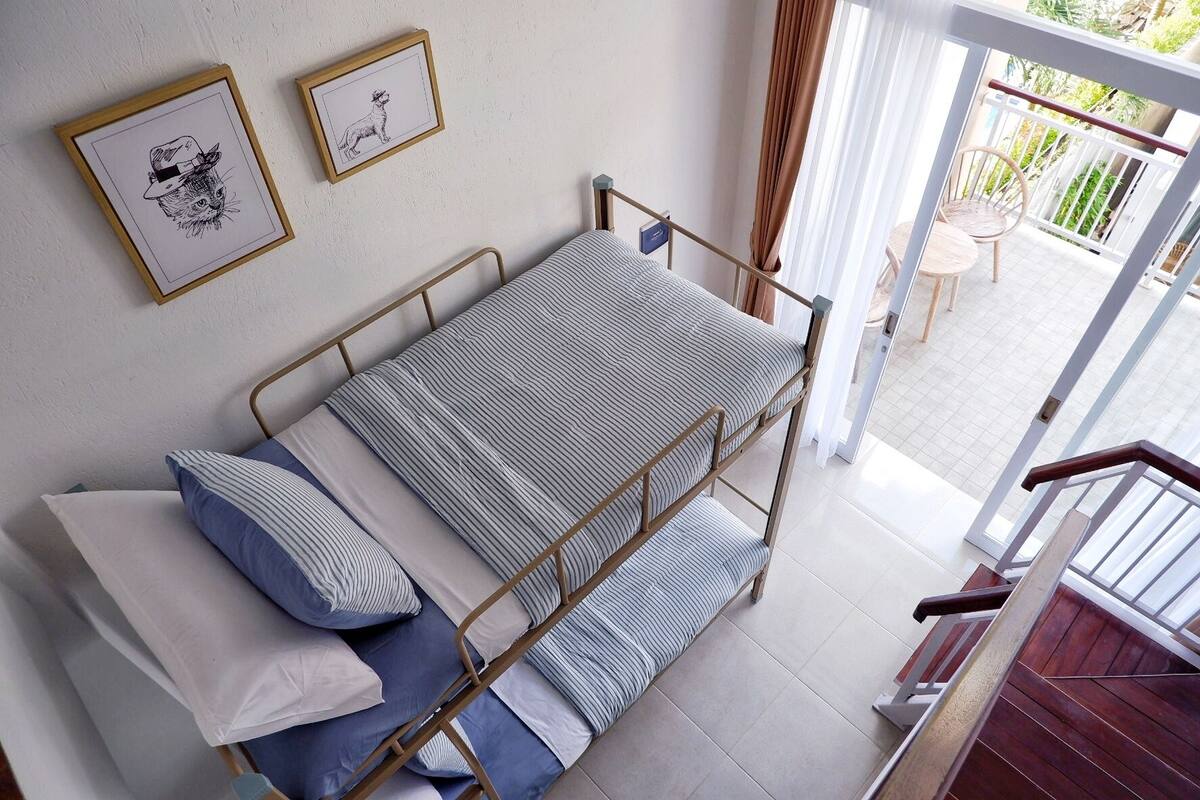 A single bed with a metal frame, striped bedding, and pillows. There are two framed pictures on the wall.