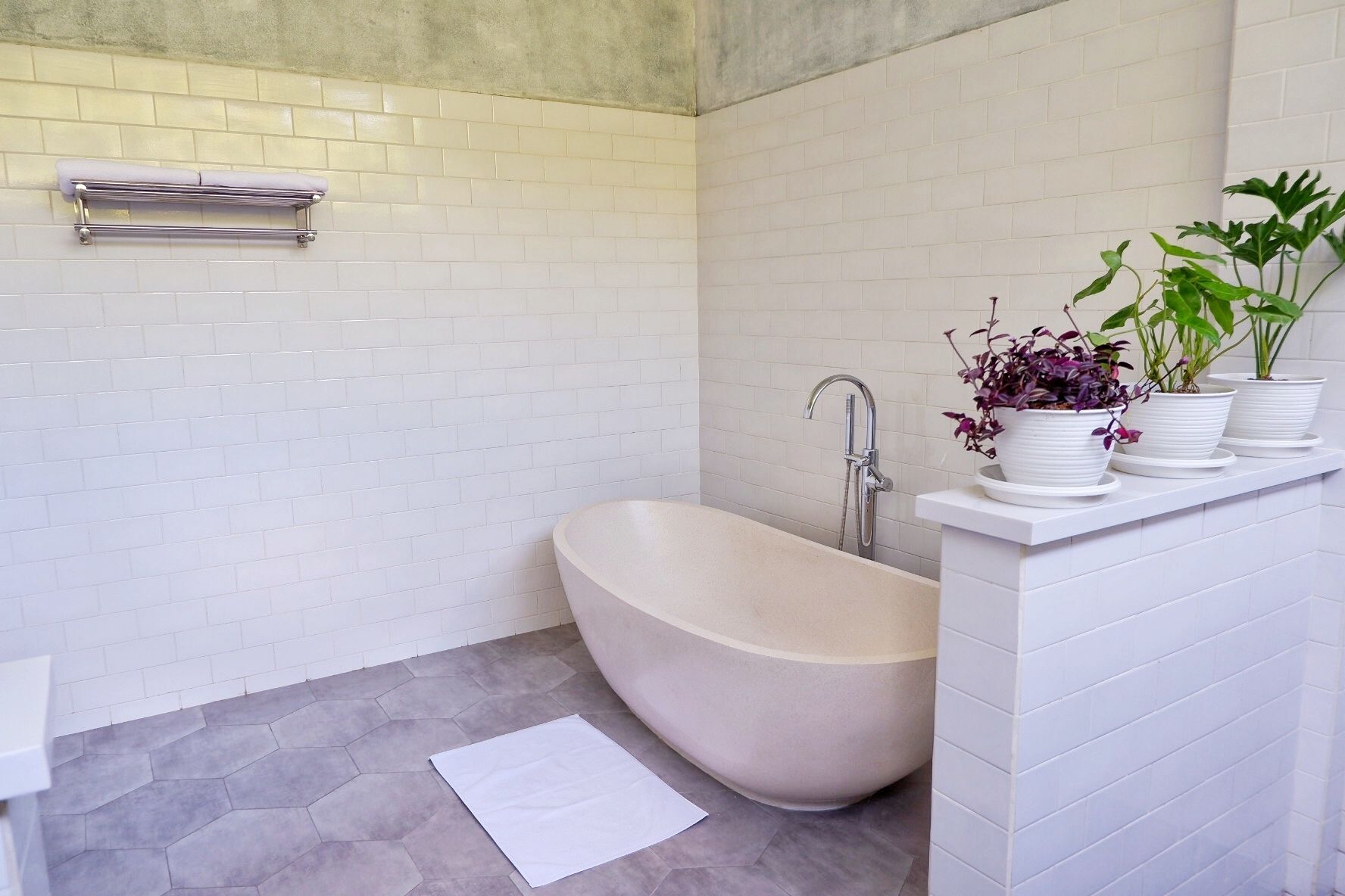 A modern bathroom with a freestanding bathtub, white tiled walls, and a shelf with potted plants.
