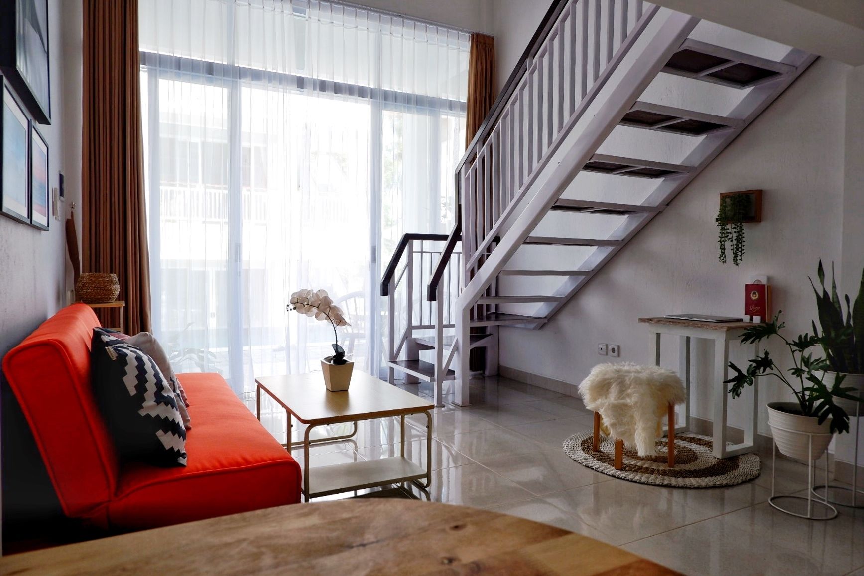 A modern living room with a staircase, a red sofa, a small table with a plant, and a fluffy rug.