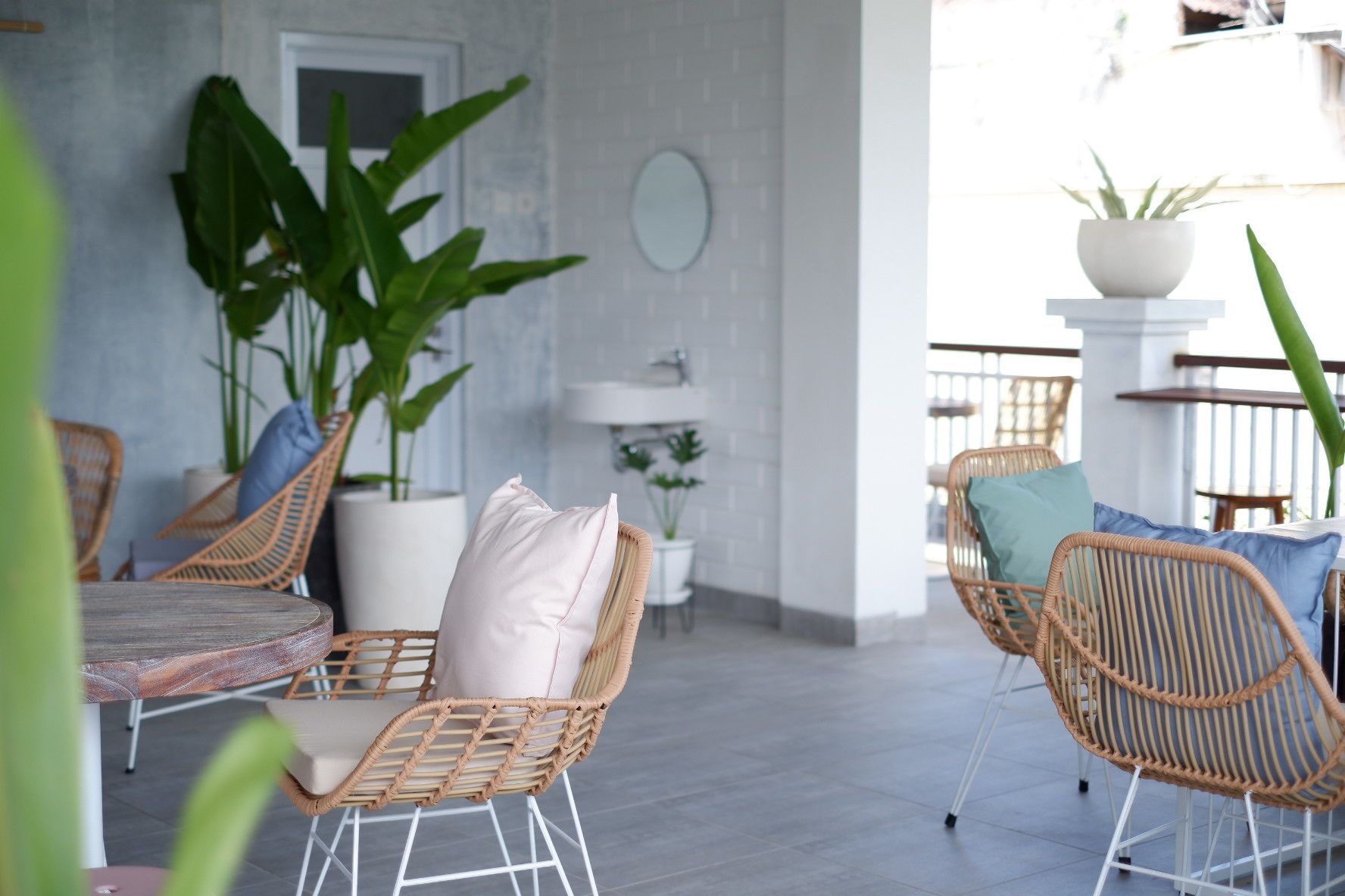 A modern outdoor seating area with wicker chairs and a round table, surrounded by potted plants and a white wall with a circular mirror.