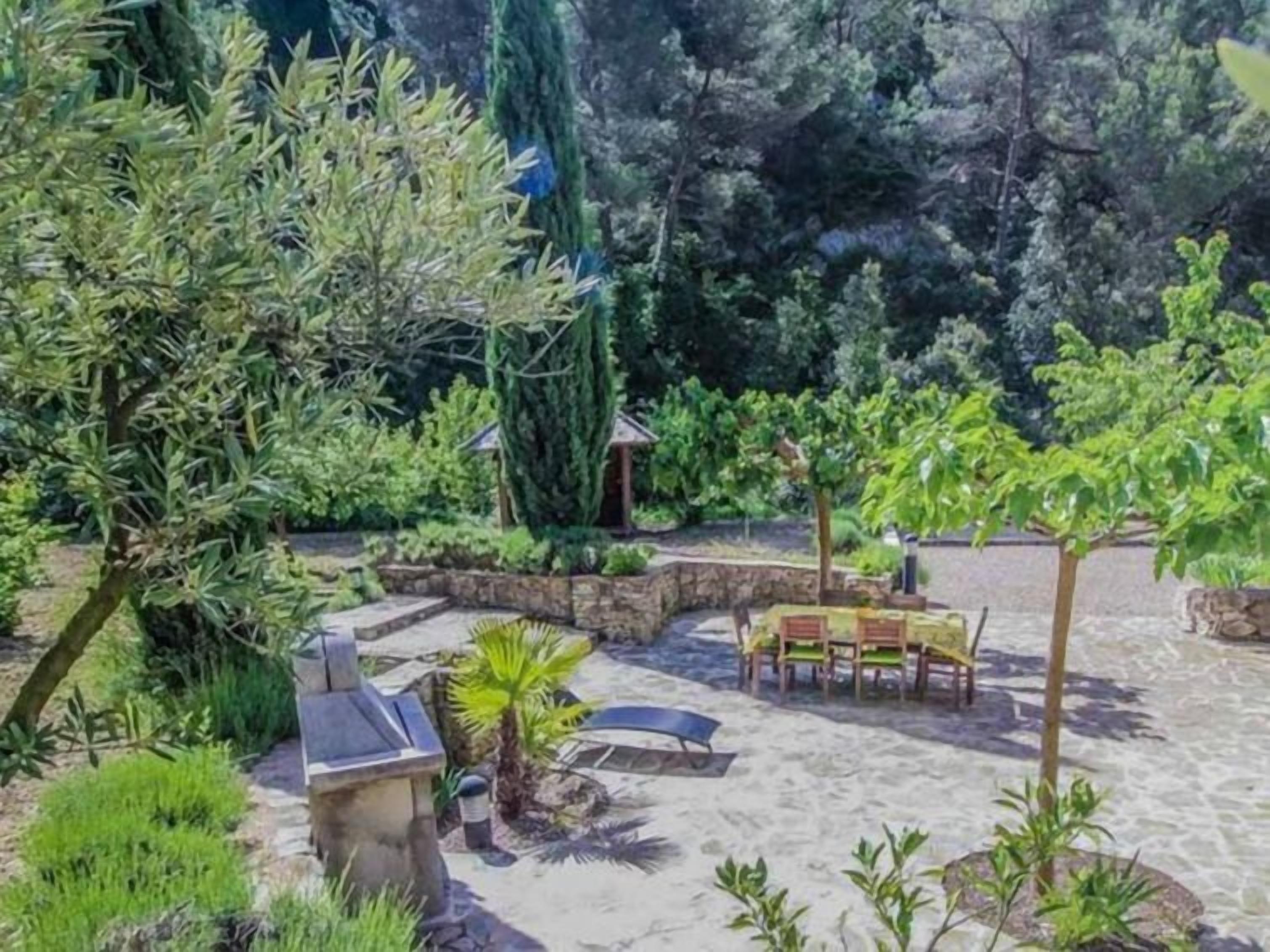 A garden with a stone bench, a small table, and a grill.