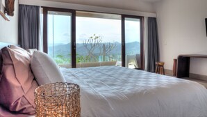 Une chambre avec un grand lit, une vue sur les montagnes et un balcon agrémenté d’un fauteuil en osier.