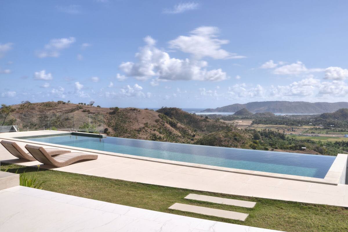 A modern infinity pool with a clear view of the surrounding landscape, including hills and a distant body of water.