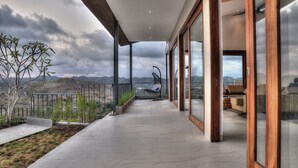 Un balcon extérieur moderne offrant une vue sur les montagnes, avec un fauteuil suspendu et un espace détente agrémenté de coussins.