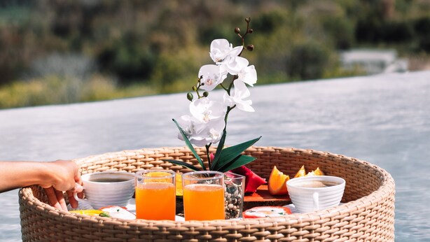 Un espace de restauration flottant avec une table en osier, du jus d’orange et une orchidée blanche.
