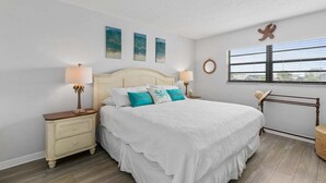 Ein Schlafzimmer mit einem Bett, zwei Nachttischen, einem Fenster mit Jalousien und Wandbildern.