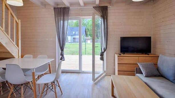 A wooden interior with a dining table, chairs, a sofa, a TV, and a sliding glass door to the outside. - TuNa (Dziwnów)