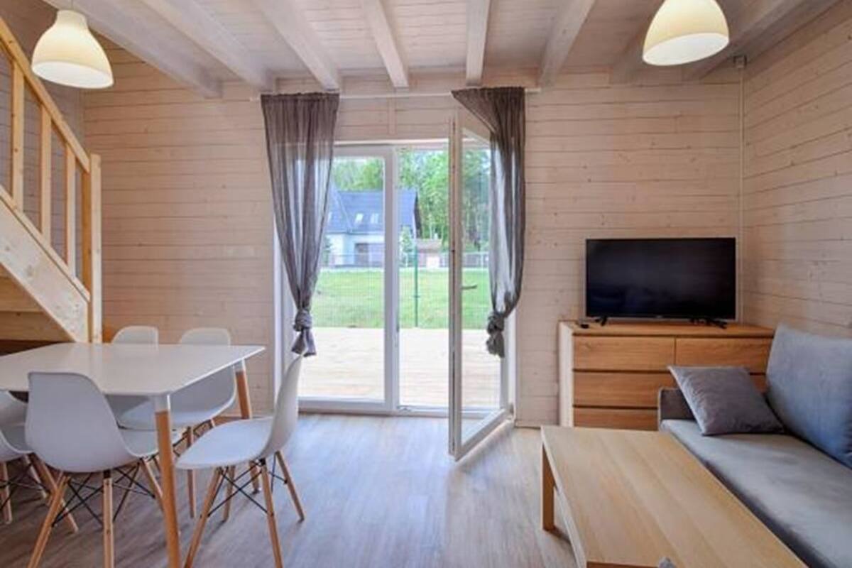 Ein Holzinterieur mit einem Esstisch, Stühlen, einer Couch, einem Fernseher und einer Glastür zum Außenbereich.