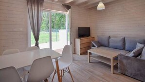 A modern living room with a wooden ceiling, a sofa, a TV, and a dining table with chairs. - TuNa (Dziwnów)
