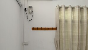 A small, clean room with a bed, white curtains, and an air conditioning unit. - Rendezvous Inn (Mandalay)