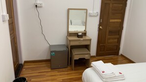A hotel room with a wooden floor, a bed with white linens, a desk with a mirror, a trash bin, and a door. - Rendezvous Inn (Mandalay)