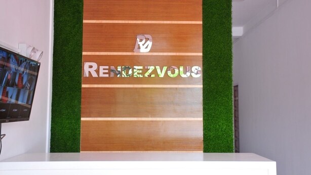 A reception desk with a wooden panel and green artificial grass, displaying the name "RENDEZVOUS". - Rendezvous Inn (Mandalay)