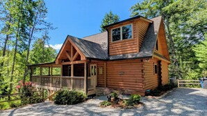A log cabin with a porch, a covered entryway, and a gravel driveway.