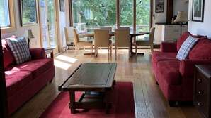 Un salón espacioso con suelo de madera, sofás rojos, una mesa de comedor con sillas y grandes ventanales con vistas a zonas verdes.