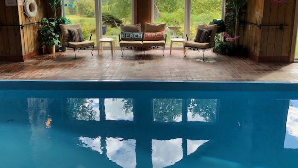 Zona de piscina con vista a un paisaje montañoso, paredes de madera y dos sillones con cojines.