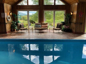 A poolside area with a view of a mountainous landscape, wooden walls, and two lounge chairs with cushions. - PRIVATE  Indoor  Pool - 10 min to VT Summer Festival -Mountain Views! (Danby)