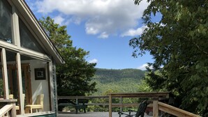 Una terraza de madera con vista a una montaña, un espacio de estar cubierto y un edificio con porche.