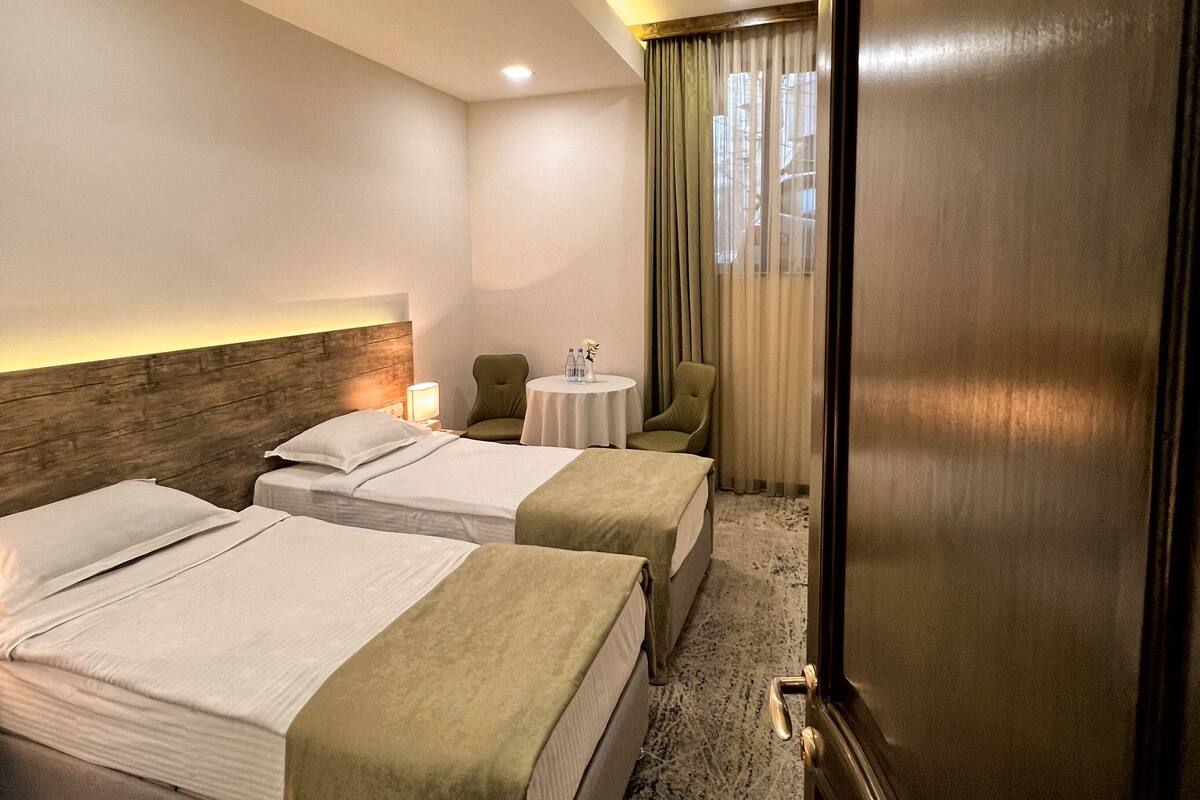 A hotel room with two beds, a wooden headboard, a small table with a lamp, and a door marked with the number 205.