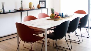 Un espace repas moderne avec une table en bois, des chaises rouges et noires, un centre de table composé de fruits et un grand tableau accroché au mur.