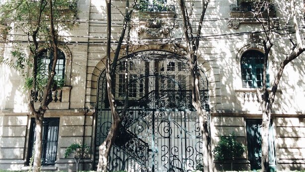 Un bâtiment historique doté de grilles en fer forgé richement décorées, d’une arche centrale et de fenêtres disposées de manière symétrique.