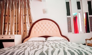 Una camera da letto con testiera capitonné, copripiumino a motivi zebrati, un comodino e una finestra con tende.