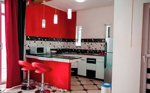 Cucina moderna con una parete di accento rossa, zoccolo di piastrelle bianche e nere e un'isola centrale con sgabelli da bar.