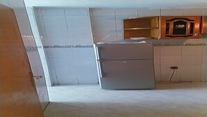 Ett kök med vita kakelväggar, ett kylskåp med två dörrar och ett träskåp ovanför diskbänken.