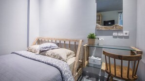 Un dormitorio con una cama, un escritorio de cristal, una silla de madera, un espejo y una planta pequeña.