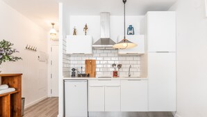 Uma cozinha moderna com armários brancos, um exaustor de aço inoxidável e uma geladeira compacta.