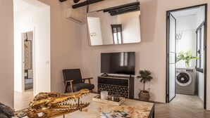 A modern living room with a large TV, a sofa, a coffee table with magazines, and a unique golden skull decoration.