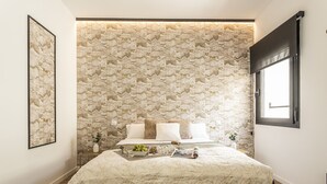A bedroom with a patterned wallpaper, a bed with white bedding, and a window with black blinds.