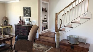 A living room with a wooden floor, a dark brown chair, a wooden chest of drawers, a bookshelf, and a staircase with a wooden railing. - 2-story house, all the comforts of home, spectacular space and views!! (Bisbee)