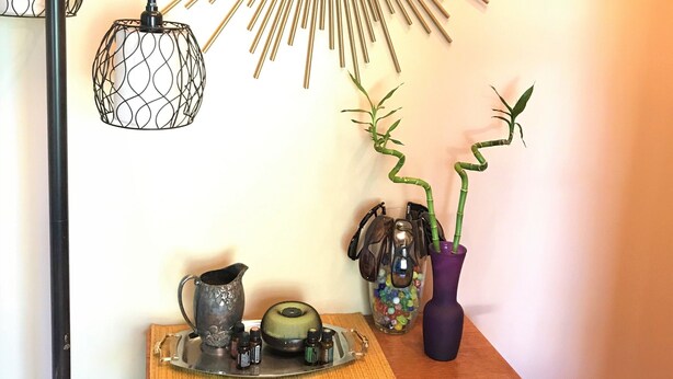 A wall-mounted mirror with a sunburst design, a wooden dresser with a vase and a small plant, and two hanging lamps. - Relax in Your Own Private Suite in Charleston's James Island! (Charleston)