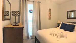 A hotel room with a bed, a nightstand, a lamp, a mirror, and a window with curtains. - Relax in Your Own Private Suite in Charleston's James Island! (Charleston)