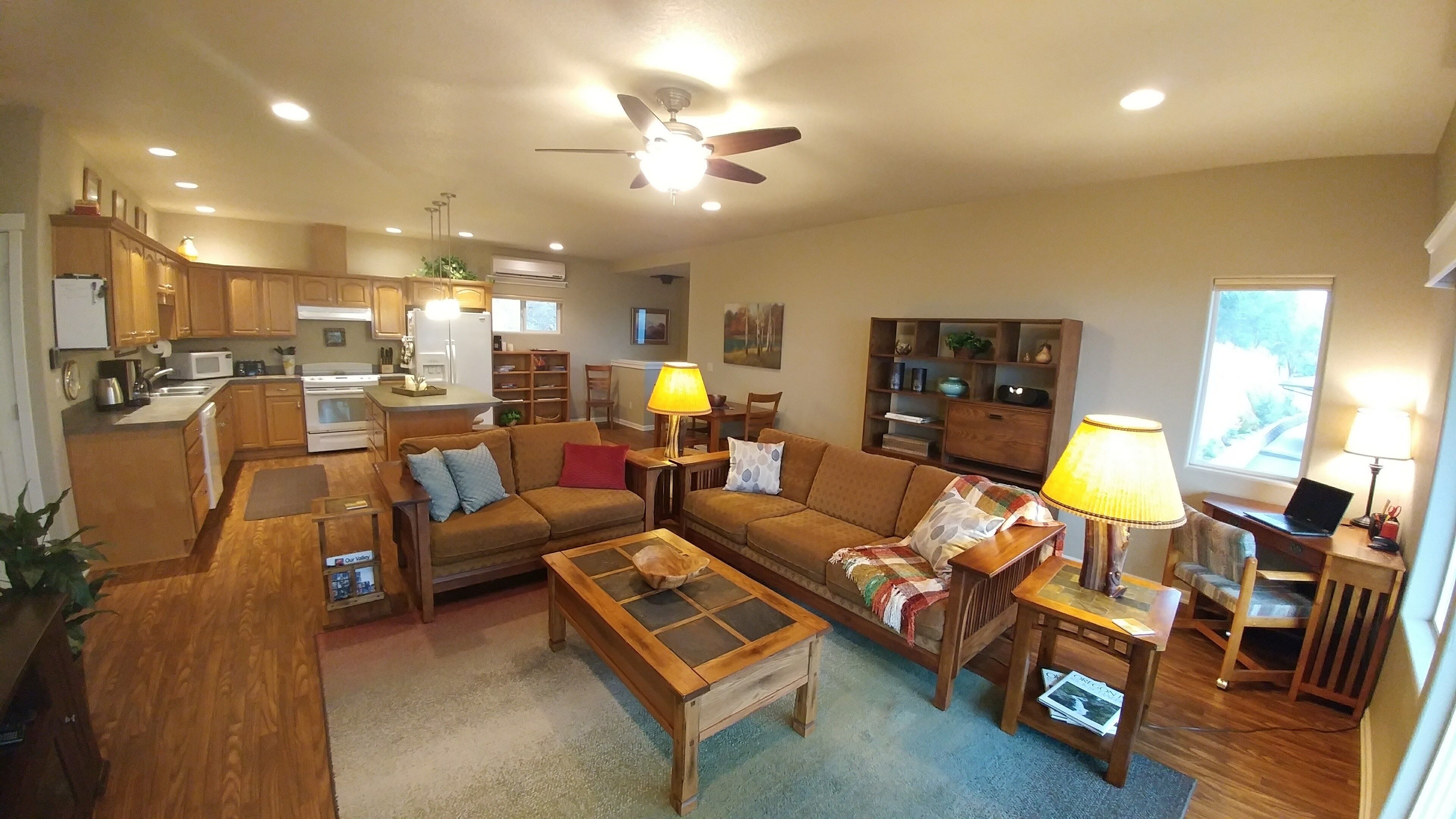 A spacious living room with a sofa, coffee table, and a dining area with a table and chairs. There is a kitchen with cabinets and appliances.