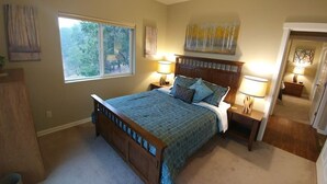 A bedroom with a large bed, two bedside tables with lamps, a window with a view of trees, and a door leading to another room. - Rogue River Guesthouse: Rural river views near I-5 (Gold Hill)
