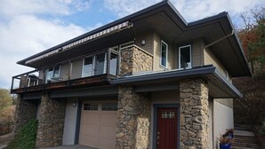 A modern two-story house with a stone facade, a red door, and a garage. - Rogue River Guesthouse: Rural river views near I-5 (Gold Hill)