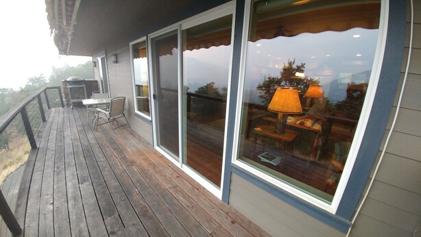 A wooden deck with a table and chairs, large windows with curtains, and a view of the landscape. - Rogue River Guesthouse: Rural river views near I-5 (Gold Hill)