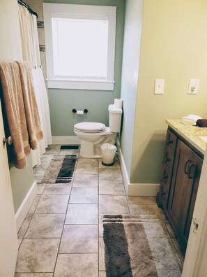 A bathroom with a toilet, a window, a towel rack, a trash can, and a cabinet.