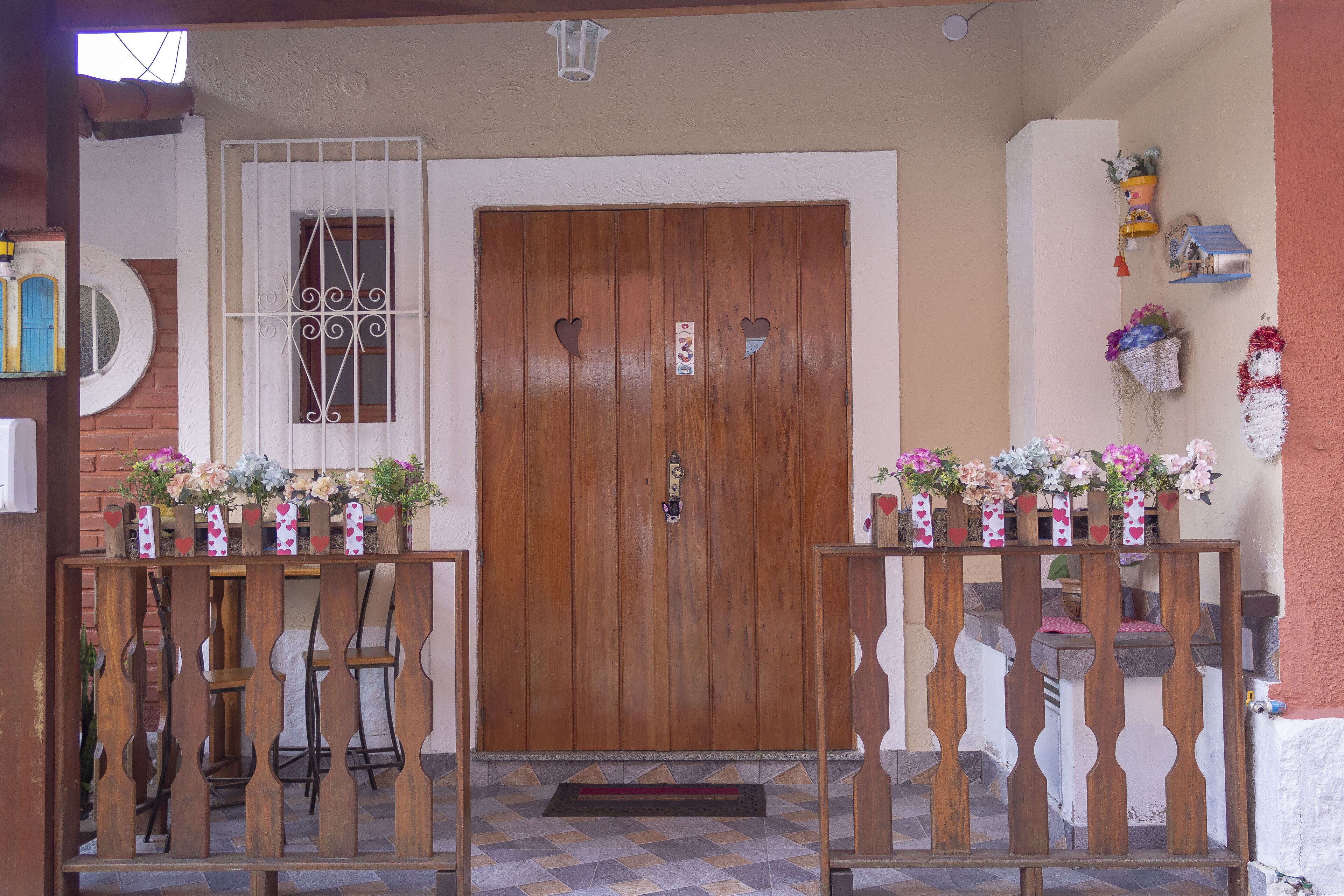 Una puerta de madera con diseños de corazones, un ventanal pequeño con rejas y un felpudo.