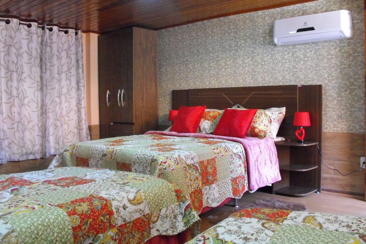 Un dormitorio con dos camas, un armario de madera, una mesita de noche con una lámpara roja y un equipo de aire acondicionado en la pared.