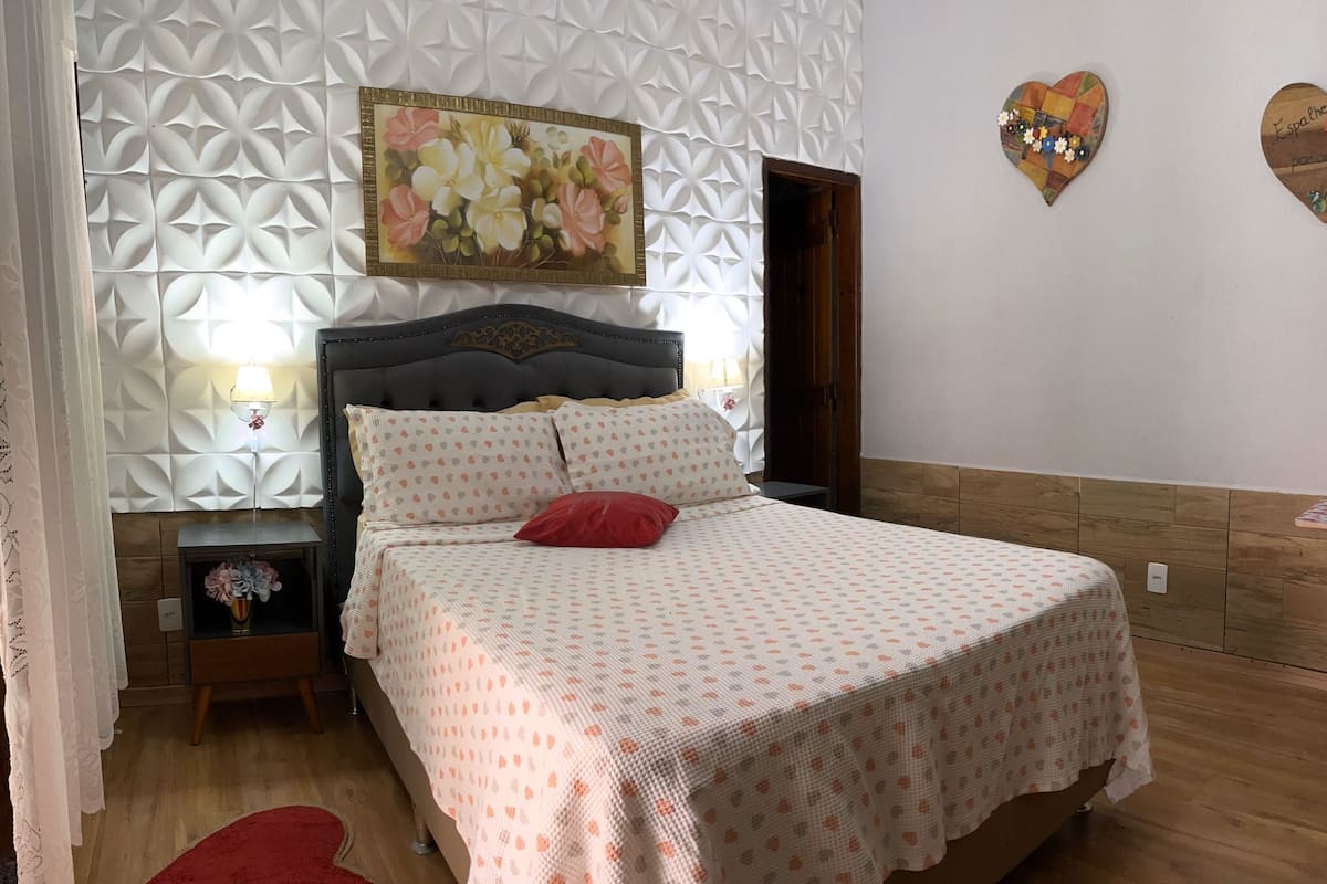 Un dormitorio ordenado con cama, mesita de noche, lámpara de pared y un panel decorativo.