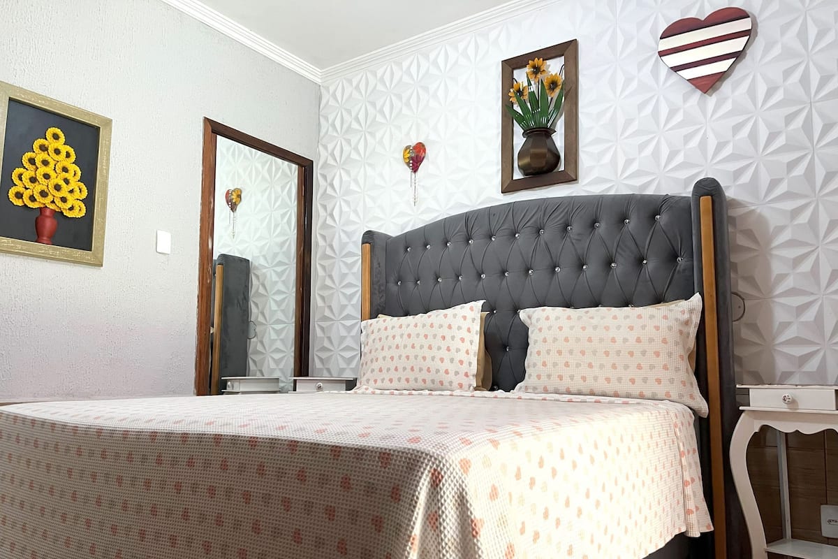 Un dormitorio con cabecera capitonada, colcha estampada, espejo y decoración en la pared.