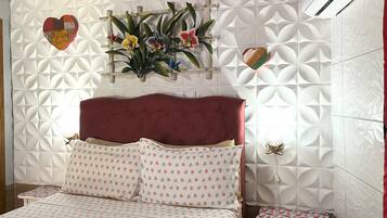A bedroom with a red upholstered headboard, a bed with patterned bedding, a small bedside table, and a wall-mounted air conditioner.