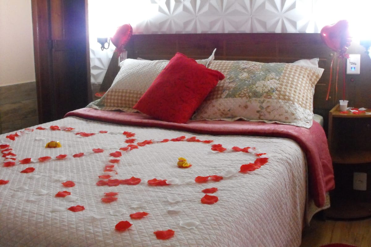 Una cama con un arreglo de pétalos de rosa en forma de corazón sobre un edredón blanco acolchado.