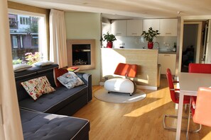 A modern living room with a sofa, a small table, and a red chair. There is a kitchen area with cabinets and a countertop.