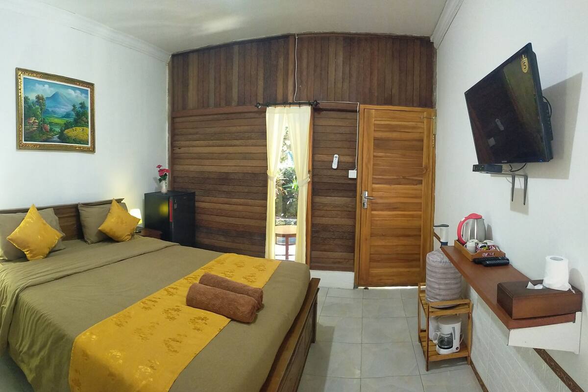 A bedroom with a bed, wooden wardrobe, TV, and a painting on the wall.